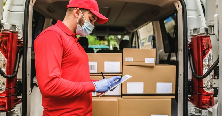 Uniformed courier in gloves reviewing delivery documentation at the rear of a loaded delivery van